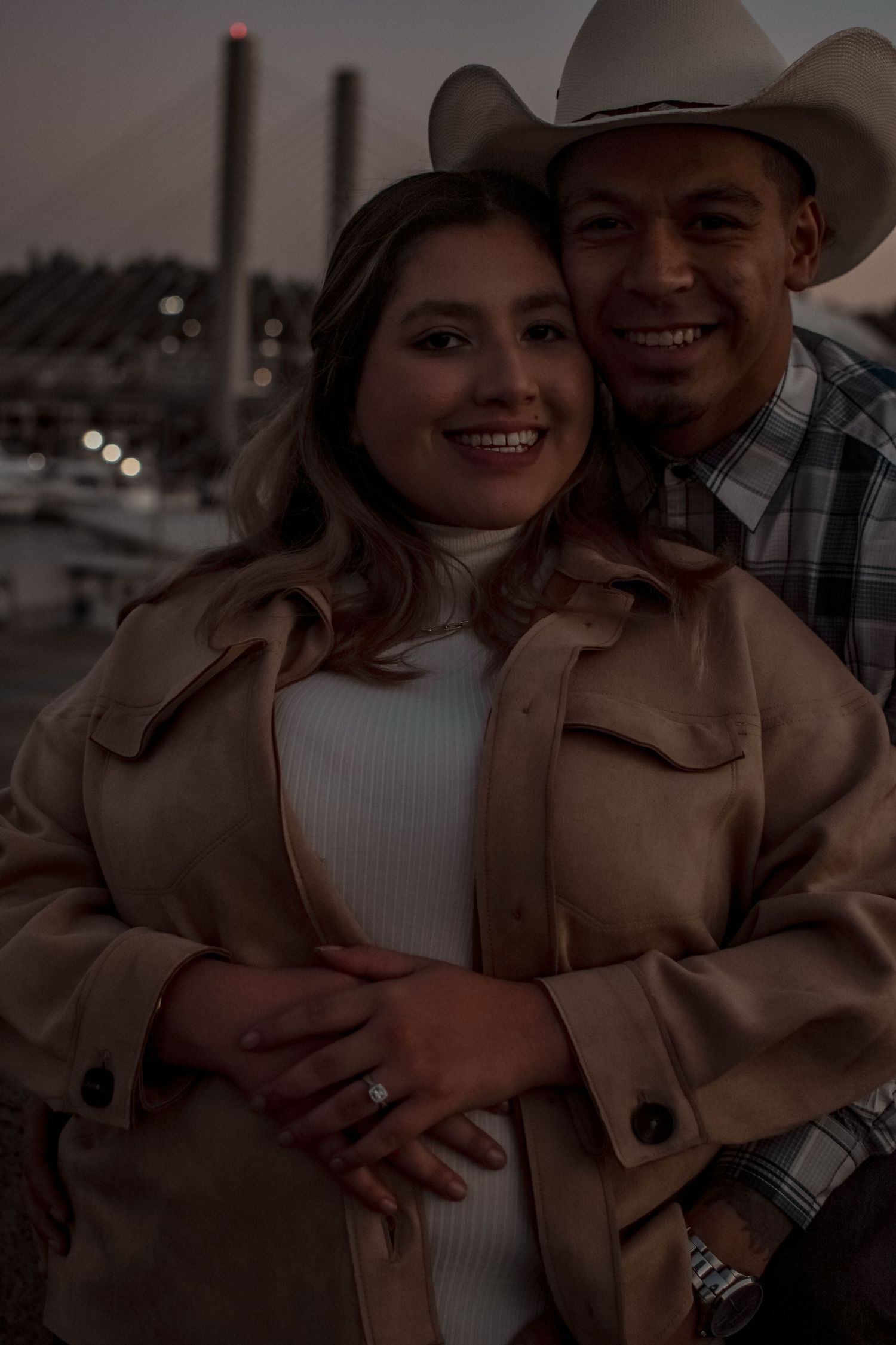 Couple in western attire embracing at dusk near a marina.