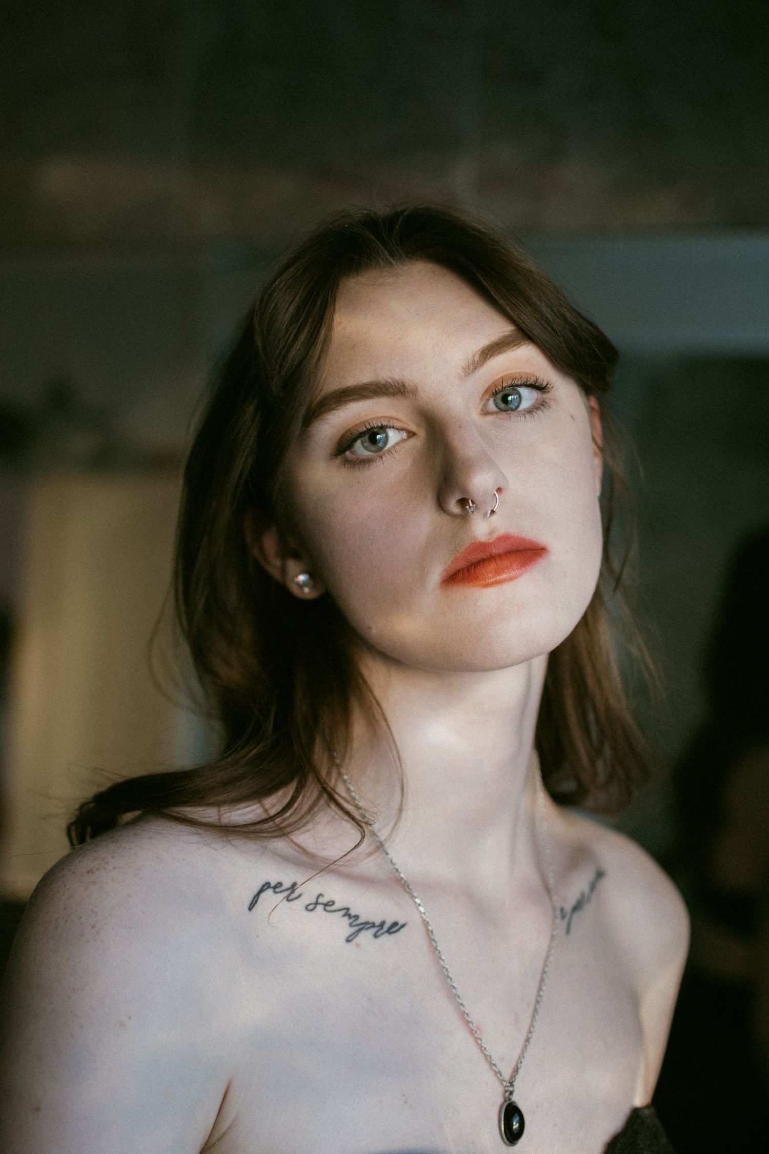Artistic portrait with moody lighting showcasing red lipstick and delicate jewelry.
