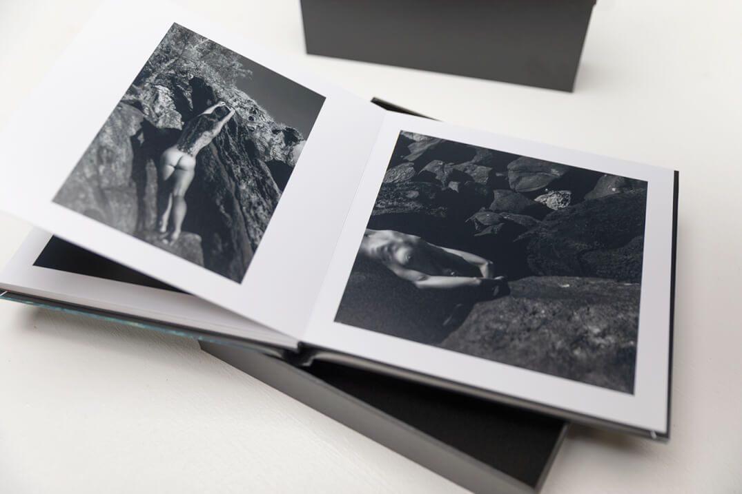 Open photography book displaying black and white artistic prints on white pages.