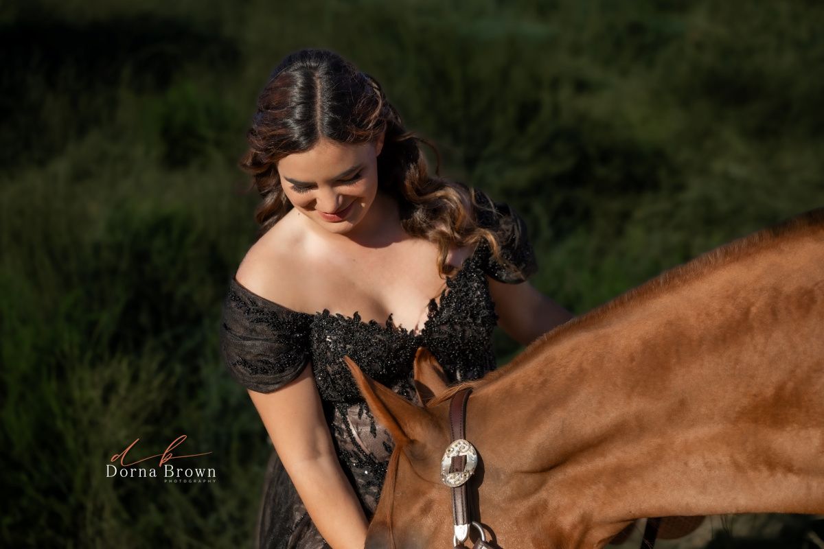 Person in black dress bonding with brown horse in outdoor natural setting.