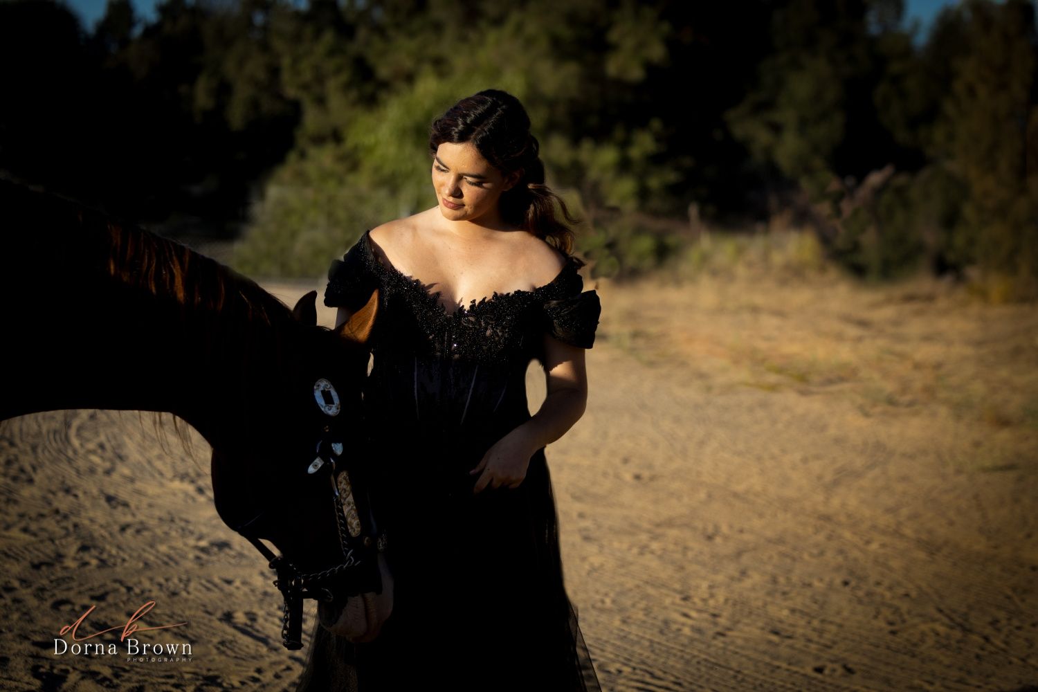 A moody outdoor portrait with a horse silhouette at sunset.