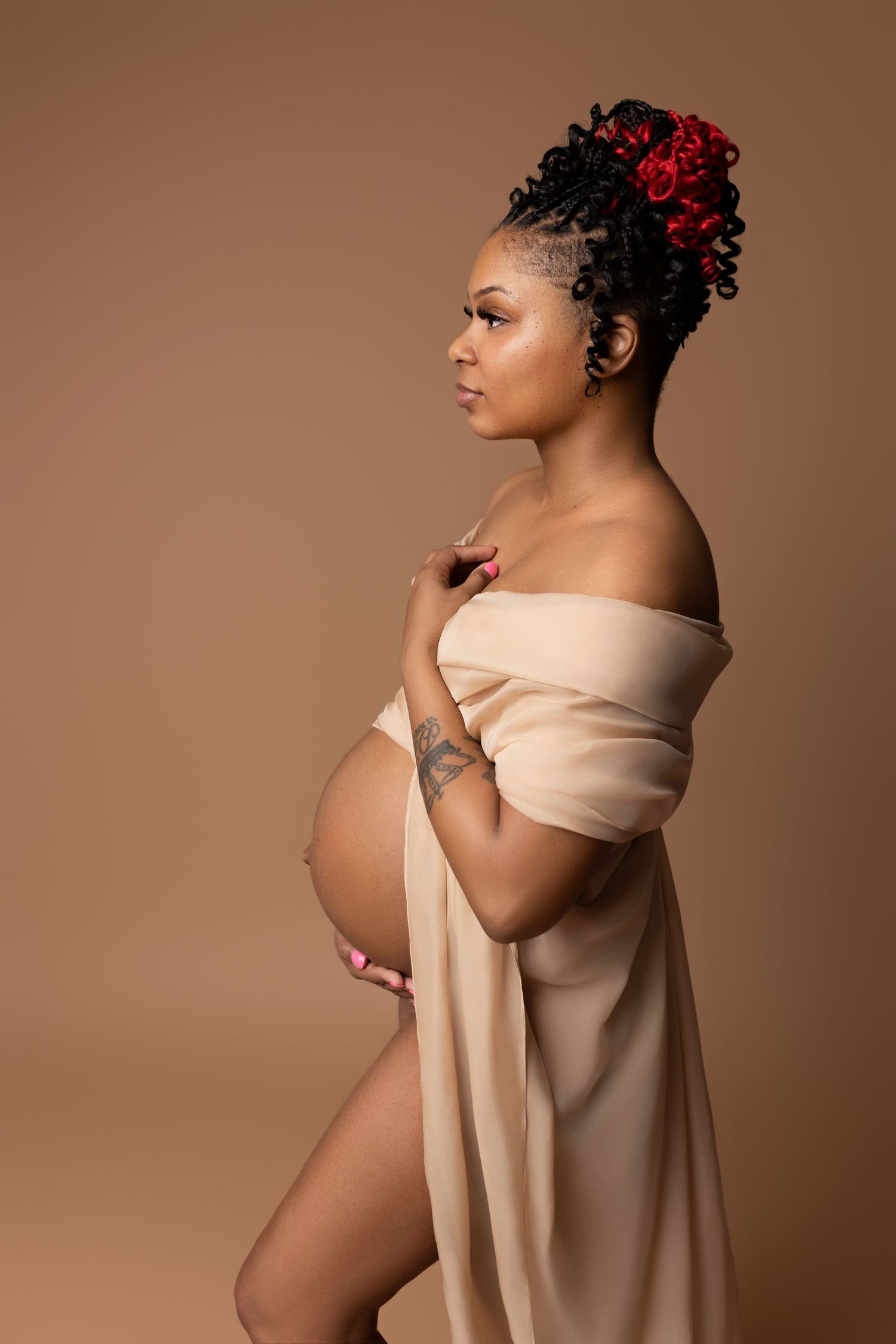Pregnant woman in a sheer champagne fabric dress, standing gracefully at our photo studio in Round Rock, TX