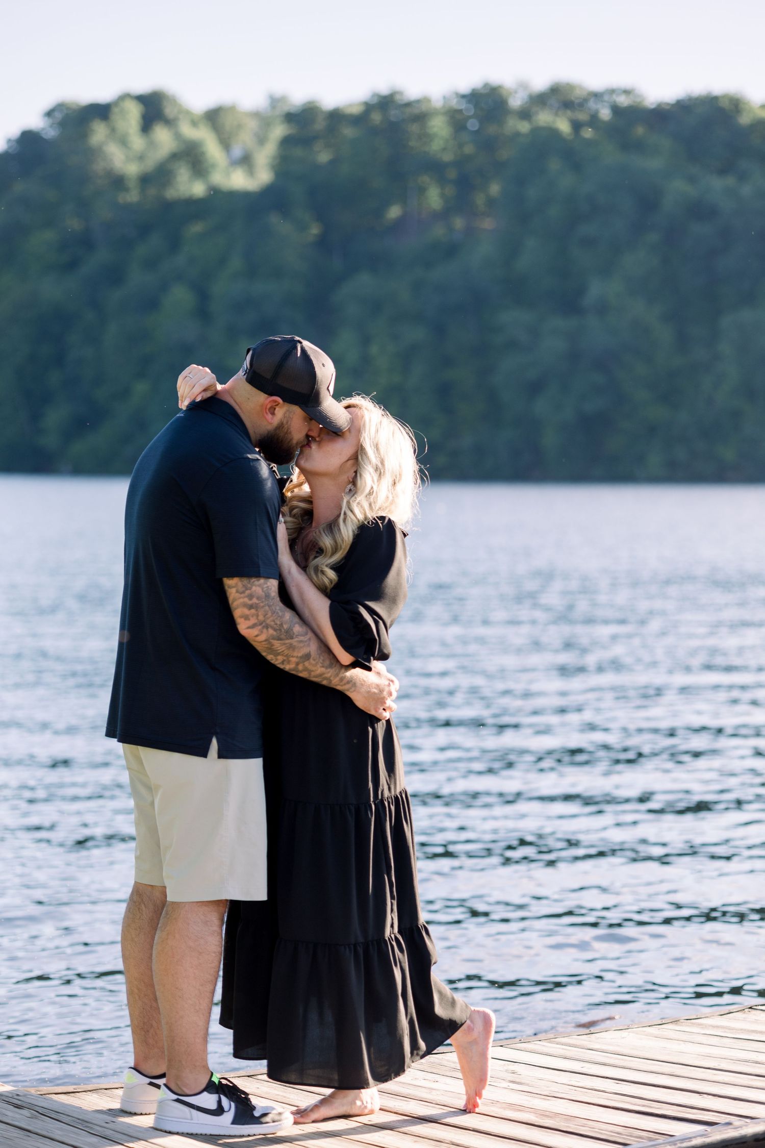 A romantic moment captured on a wooden dock by a lake with trees in the background.