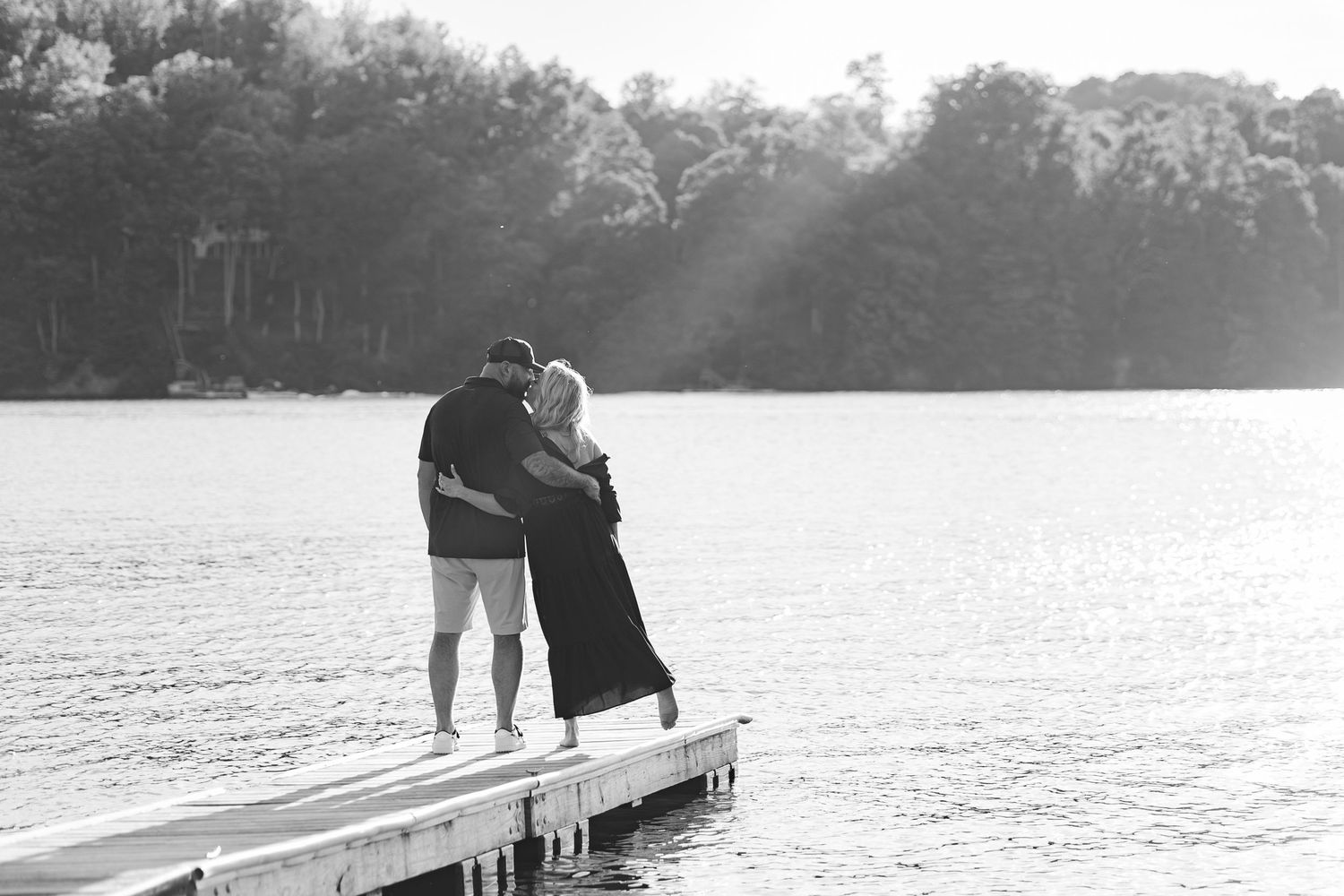 Silhouettes of a couple embracing on a lakeside dock during sunset.