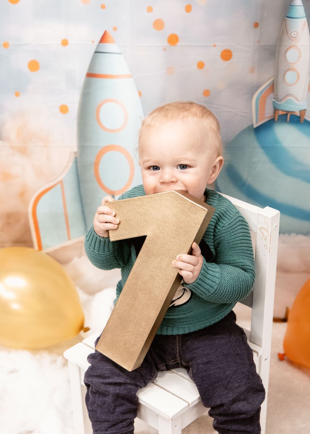 First birthday photo shoot with child holding large number one prop against rocket ship backdrop.