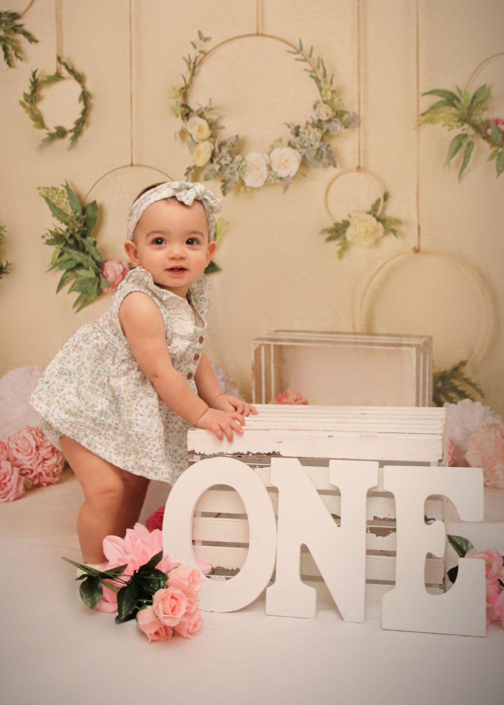A floral themed first birthday setup with white ONE letters and hanging botanical wreaths.