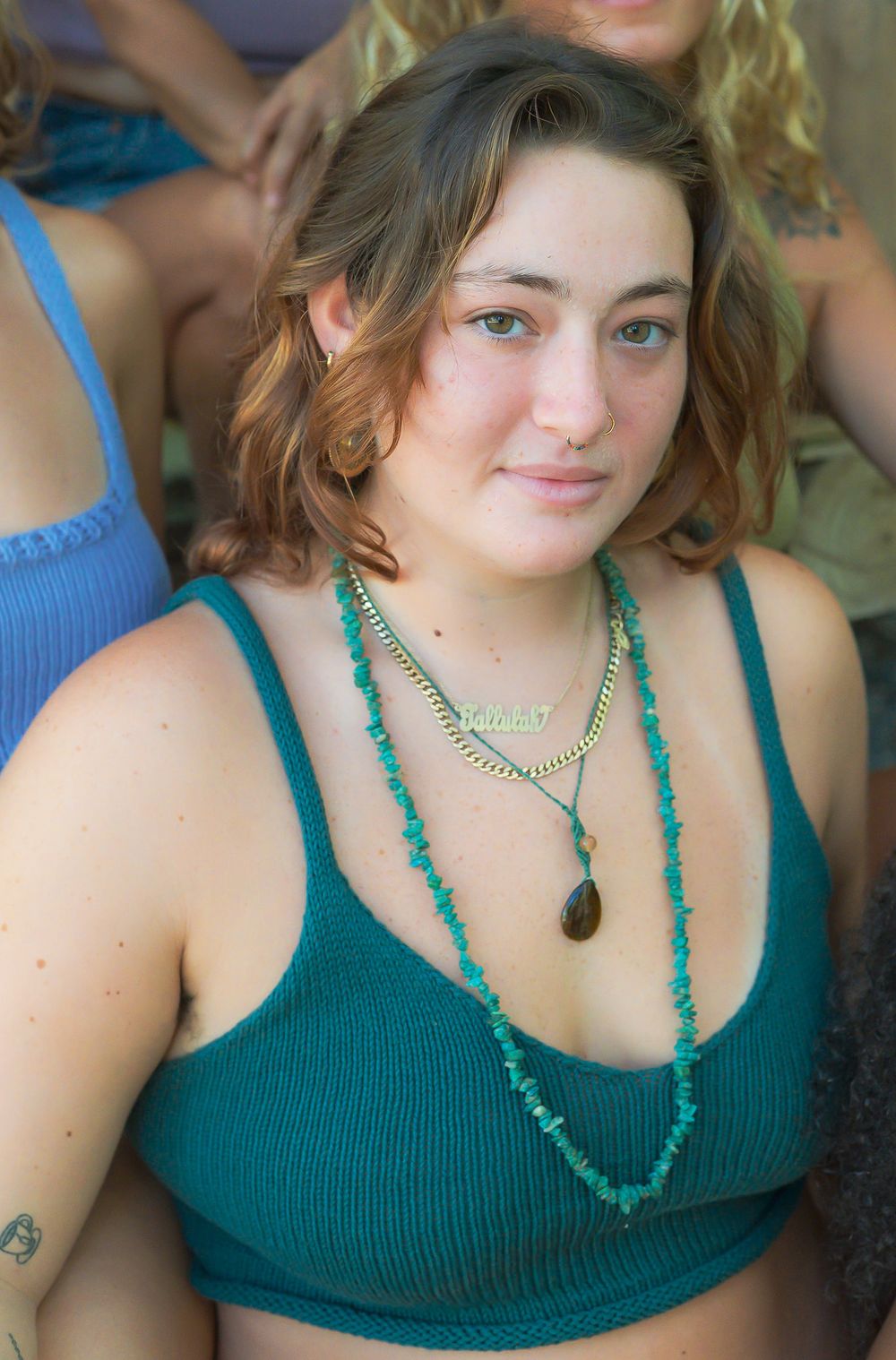 Person wearing teal knit top with turquoise stone necklaces in natural lighting.
