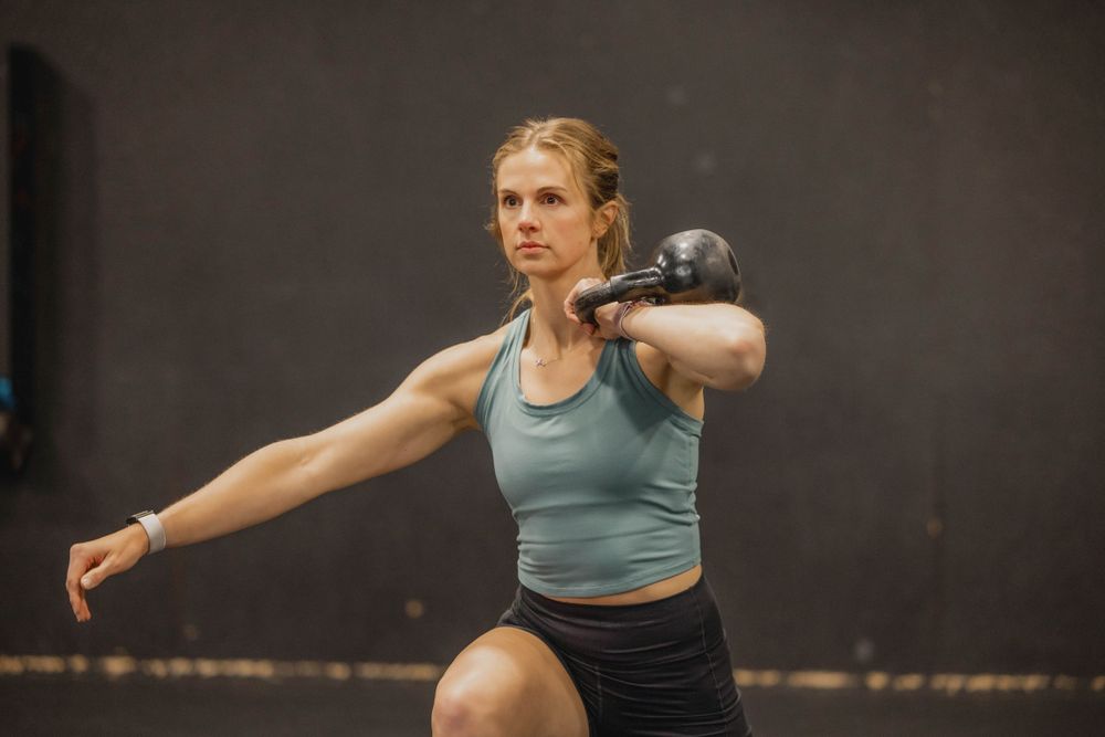 Athlete performing a kettlebell exercise in a dark gym setting.