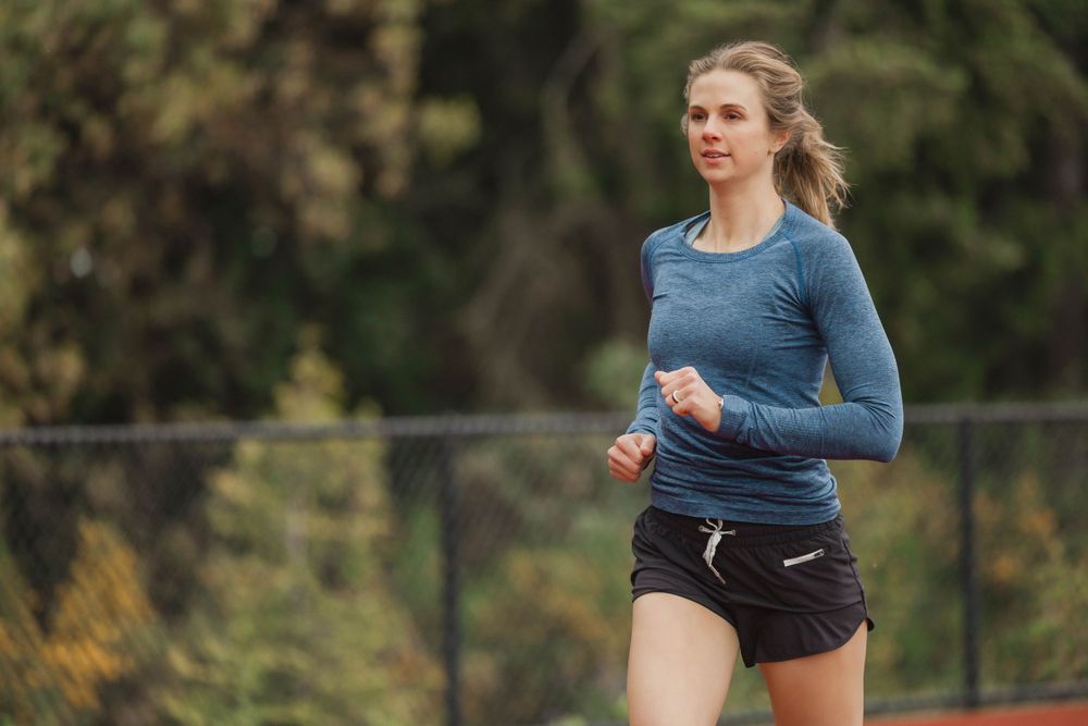 Runner in blue long sleeve shirt and black shorts jogging on an outdoor track.