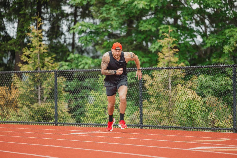 Runner in orange beanie training on a red track with trees in background.