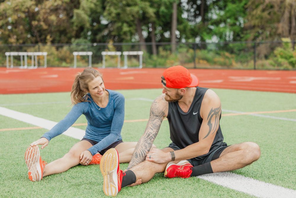 Two athletes stretching on artificial turf field during outdoor workout session.
