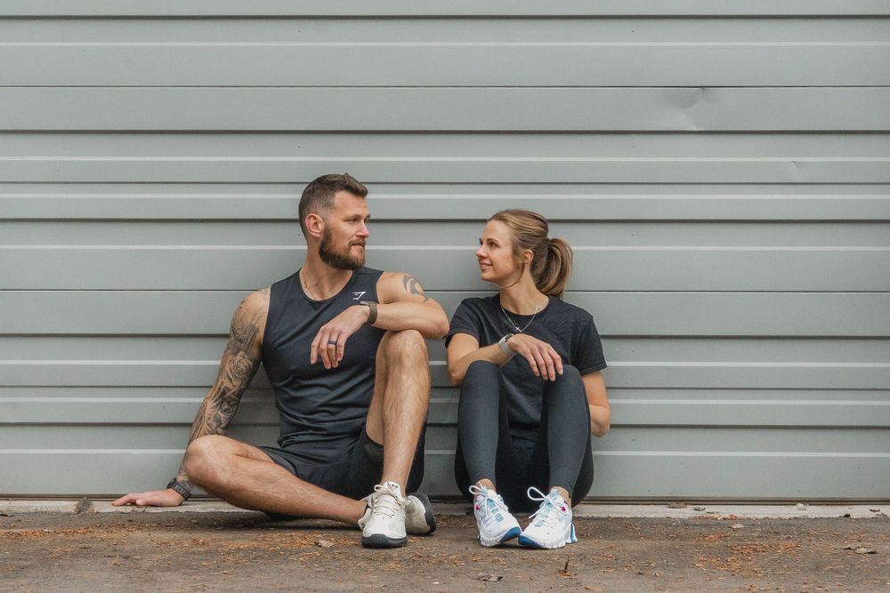 Athletic duo sitting and chatting against industrial grey wall background.