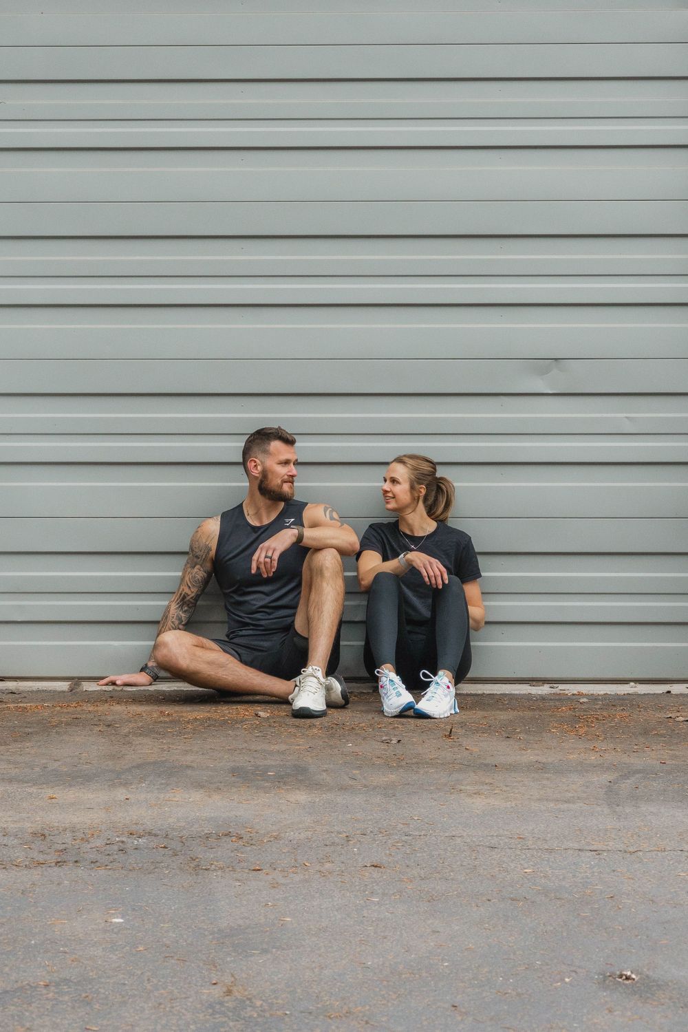 Two athletes sitting and relaxing against an industrial gray wall after workout.