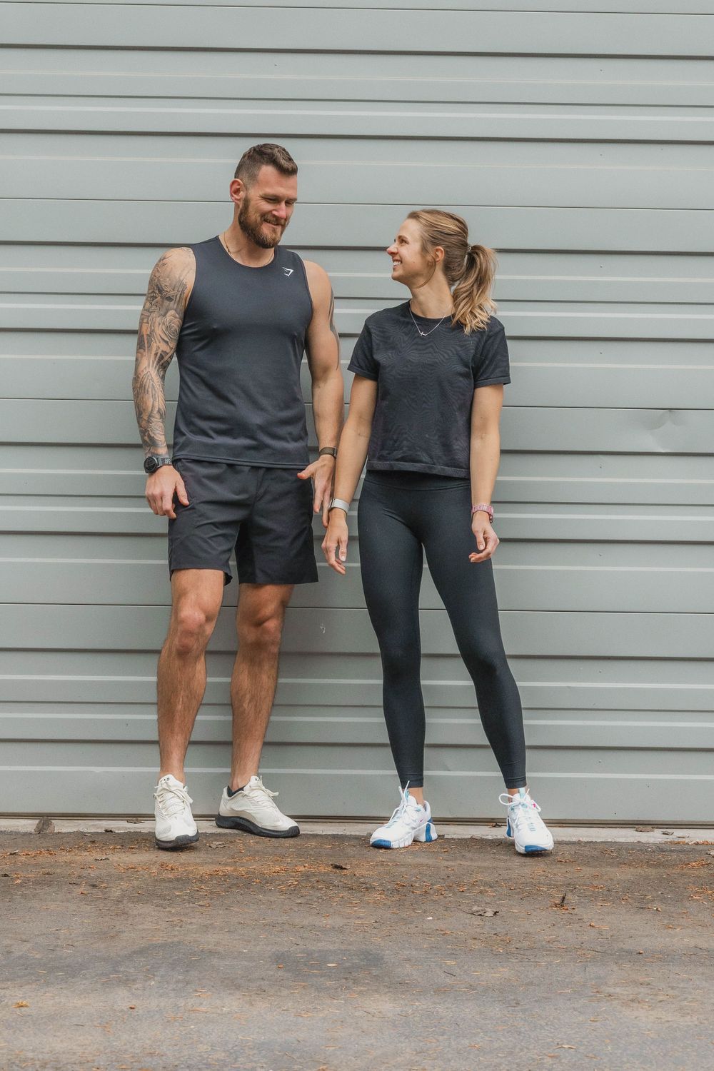 Athletic couple in matching workout gear standing against a gray wall.
