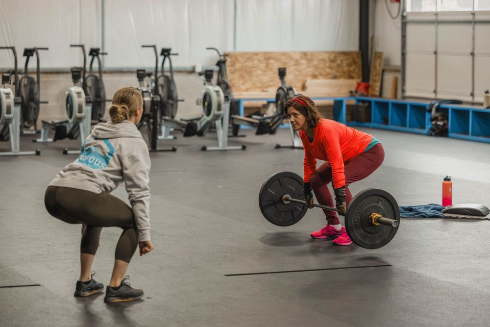 Two athletes practicing deadlifts with barbells during CrossFit-style workout.