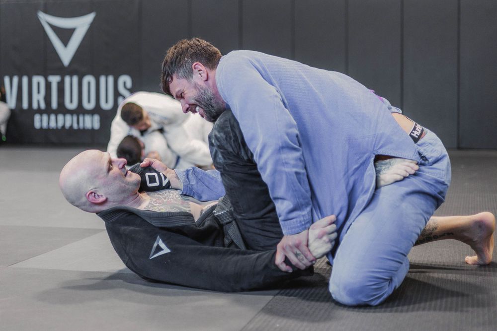 Two practitioners demonstrating Brazilian Jiu-Jitsu techniques on training mats at Virtuous gym.