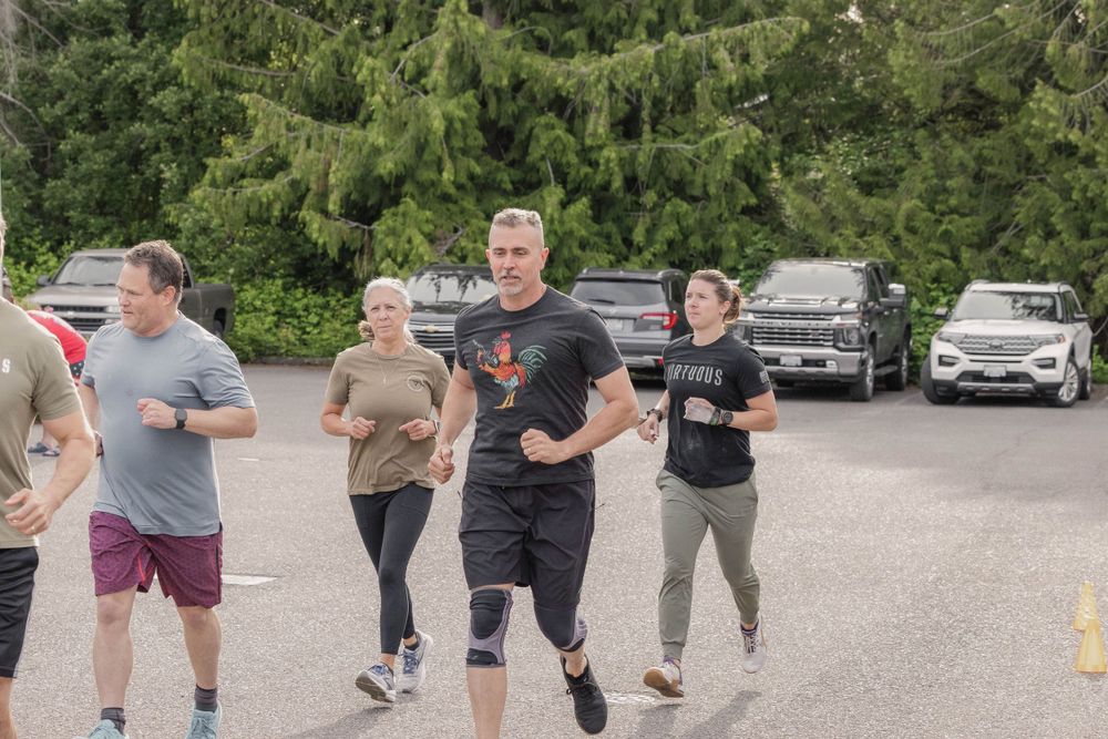 Group of people jogging together in a parking lot surrounded by trees.