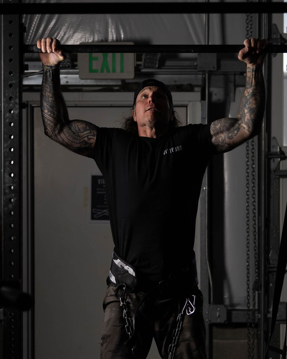 Athletic person performing pull-ups on a gym rack under dark lighting conditions.