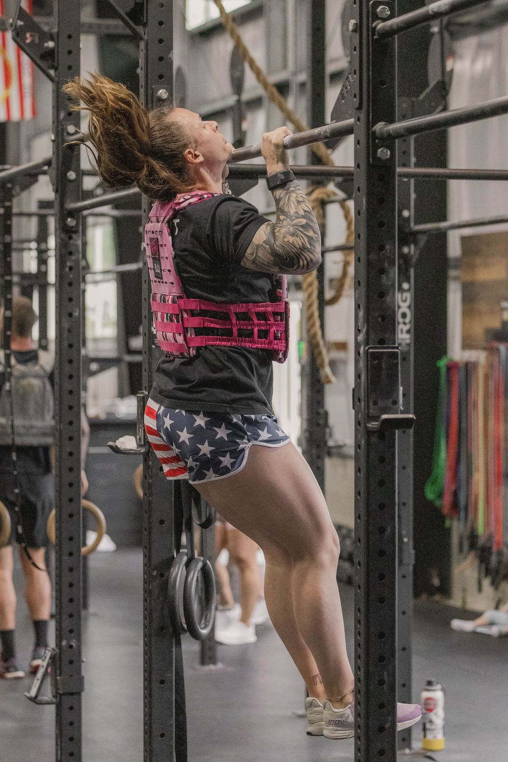 Athlete doing pull-ups wearing patriotic workout gear in a CrossFit gym.