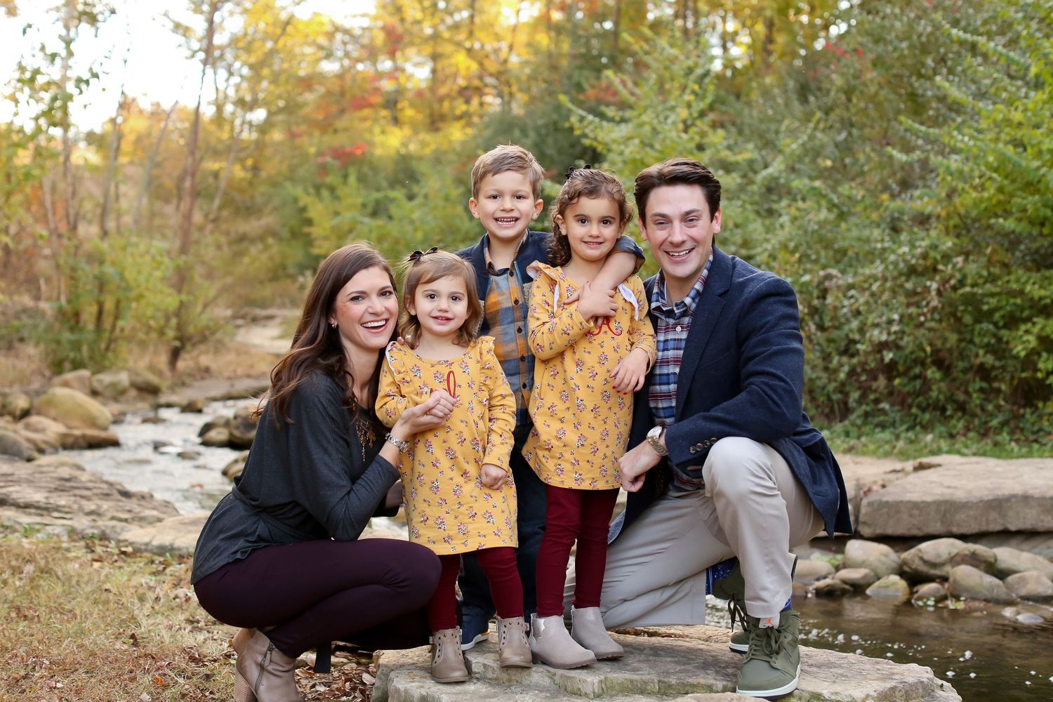 Family portrait by creek with autumn foliage and rocks in background.