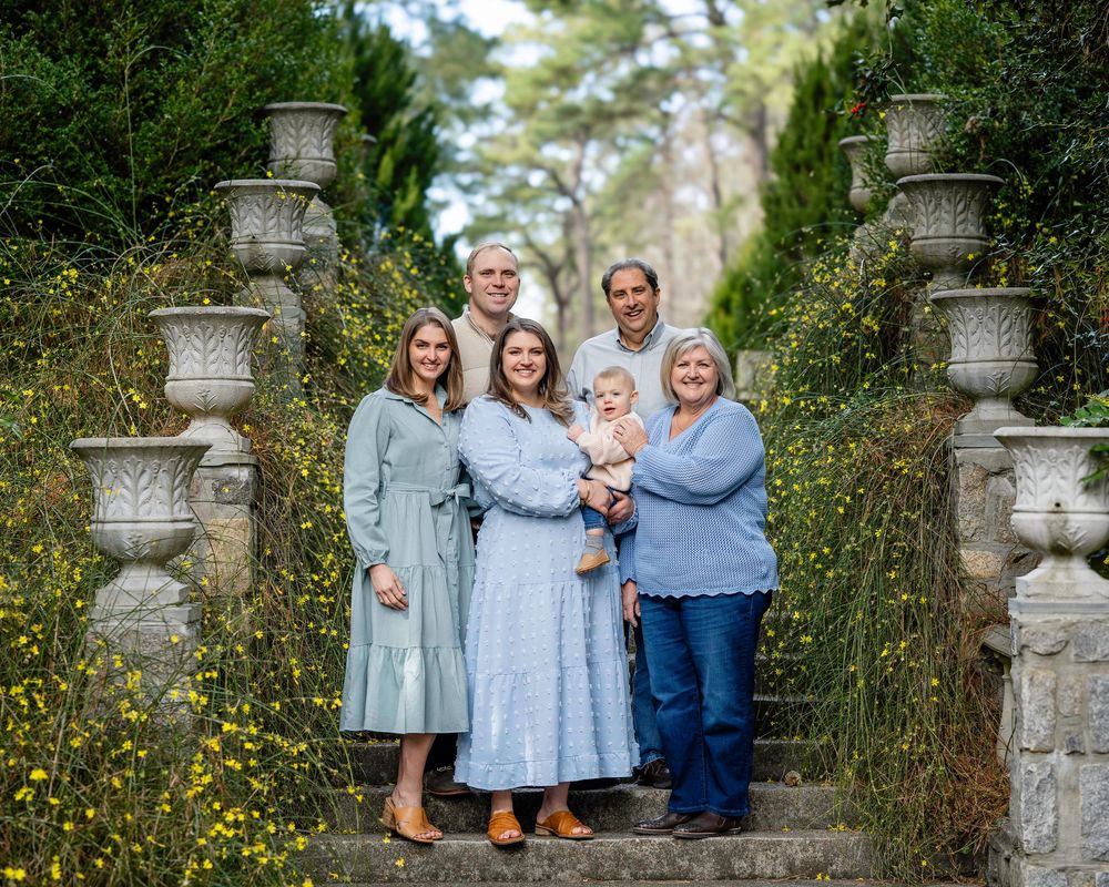 A family poses on stone garden steps flanked by ornate pillars among blooming yellow wildflowers.