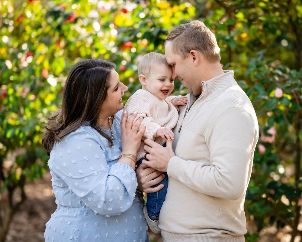 A family shares tender moments together in an outdoor setting with autumn foliage in the background.