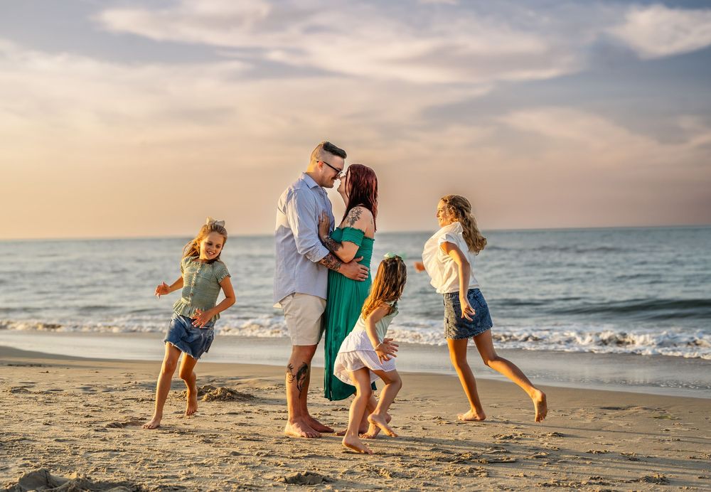 Family enjoying a playful moment together walking and running on a sandy beach at sunset by the ocean waves.