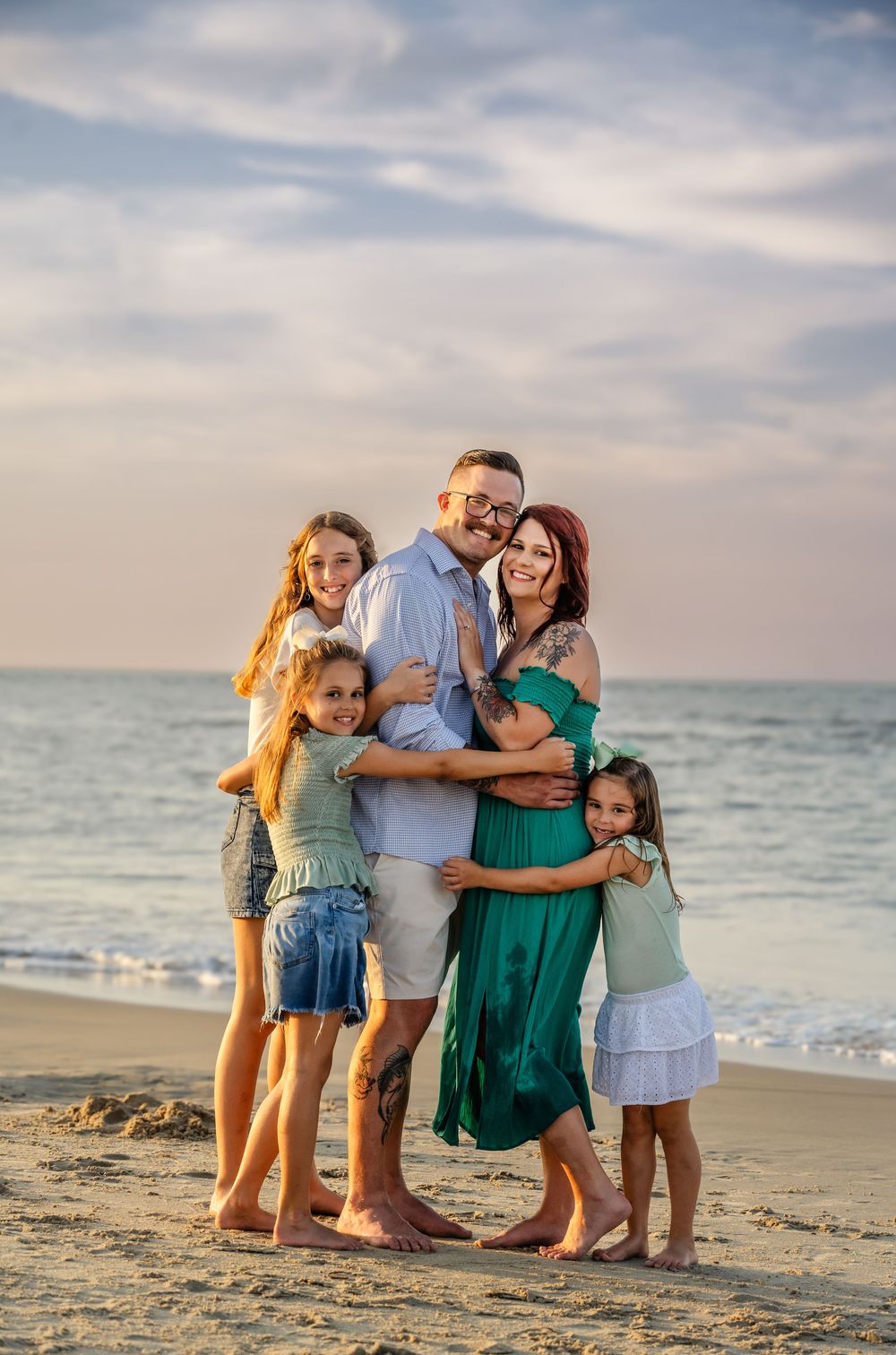 A group embracing at sunset on a sandy beach with ocean waves and cloudy sky in the background.