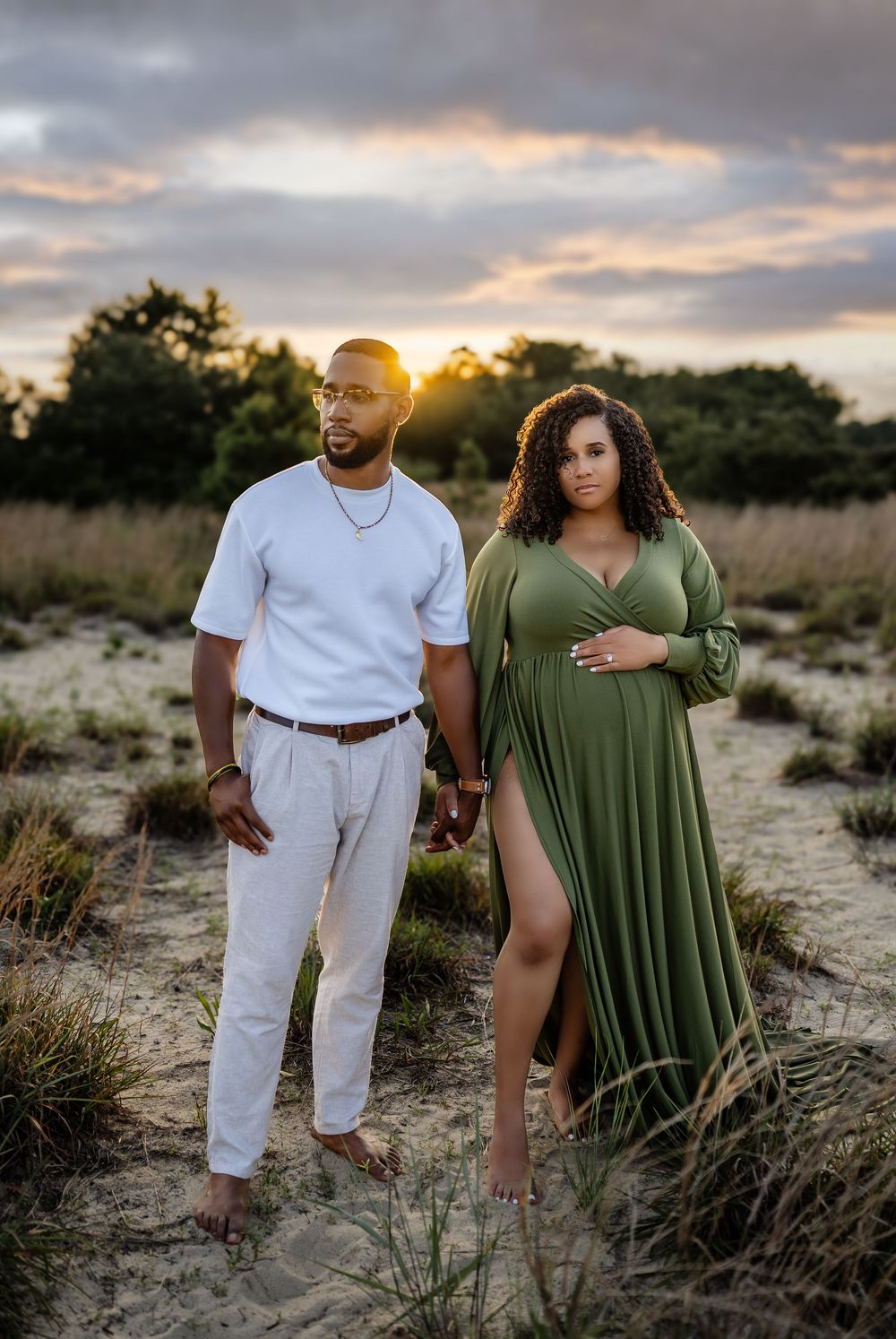 A couple stands together in a rustic outdoor setting with desert brush at sunset creating a romantic atmosphere.