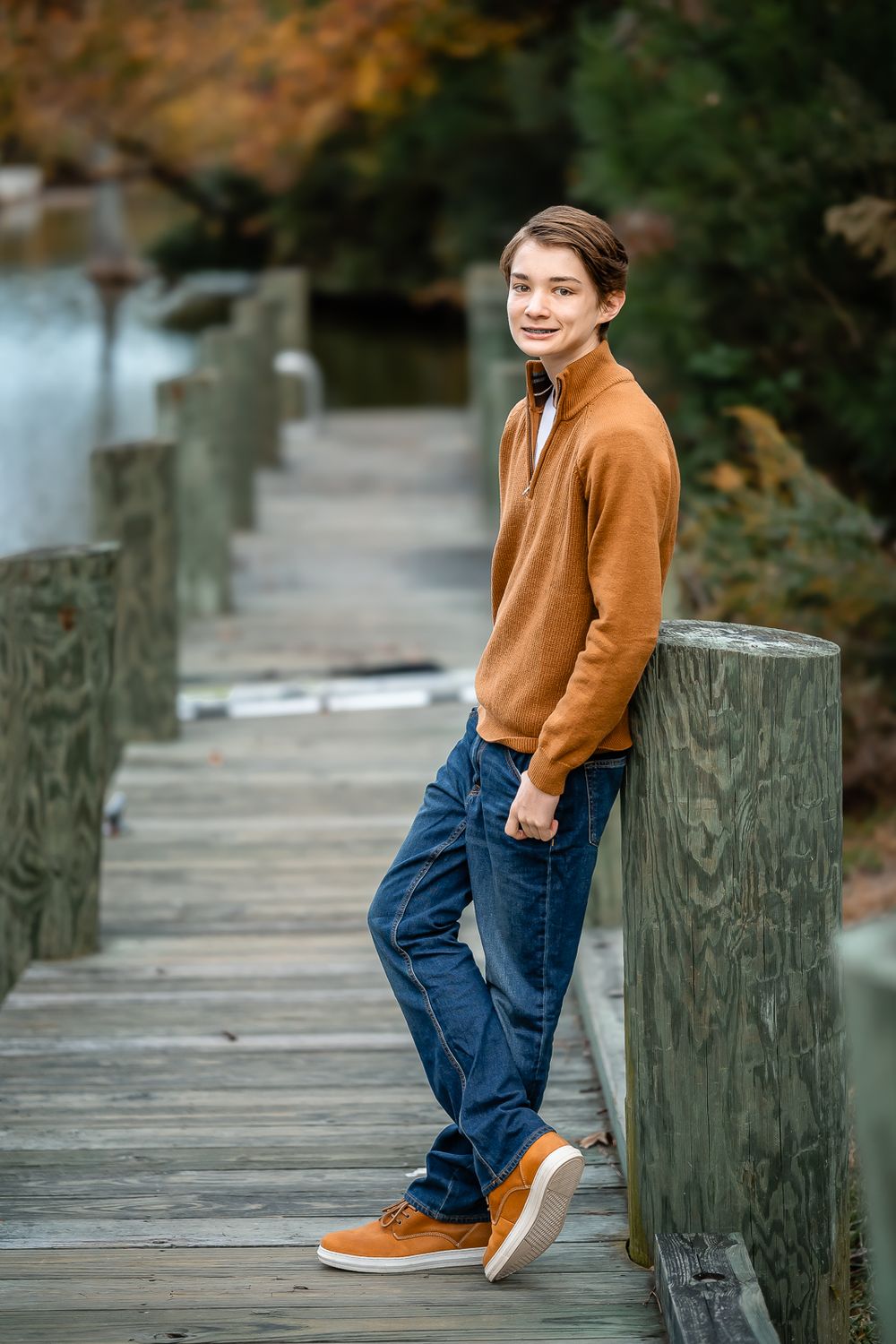 Casual outdoor portrait on wooden boardwalk wearing brown sweater and jeans during fall season.