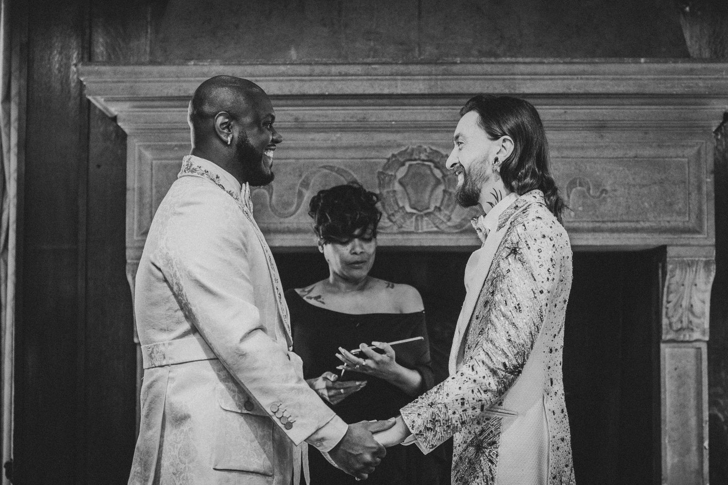 A black and white wedding ceremony photo showing a couple joining hands during their vows.