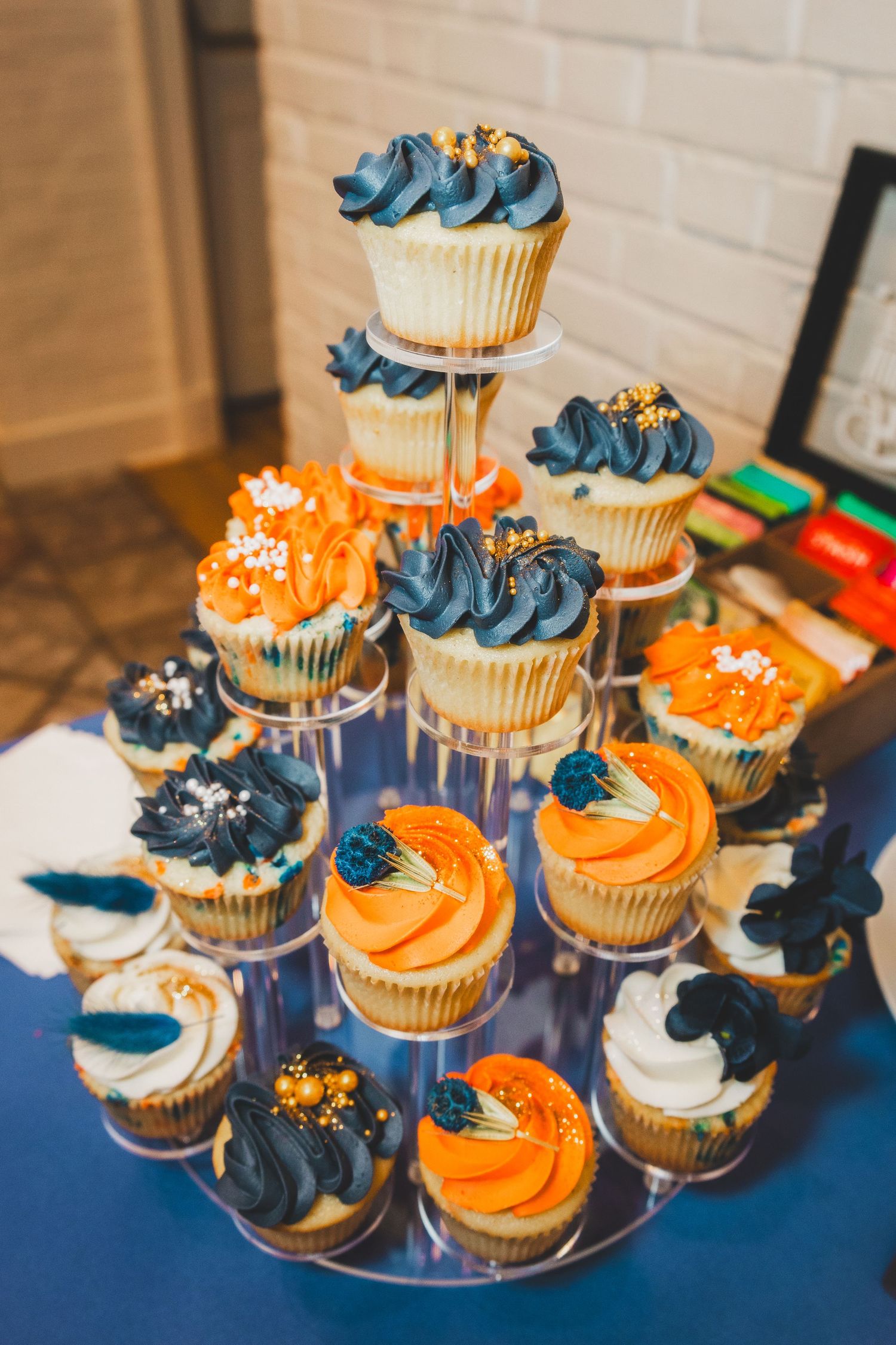 Cupcake tower decorated in blue and orange frosting arranged on tiered display stand.