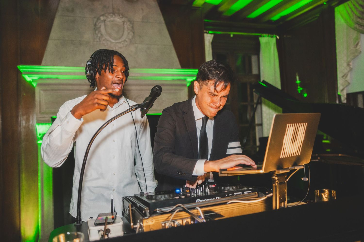 DJs performing at event with professional equipment and green lighting effects.