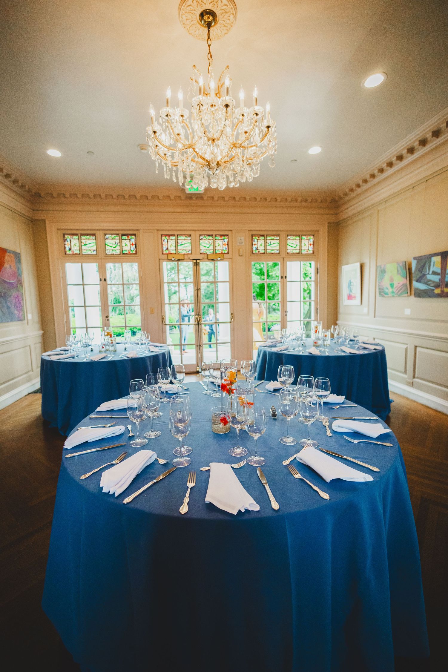 Formal dining table with blue tablecloth set for elegant dinner under crystal chandelier.