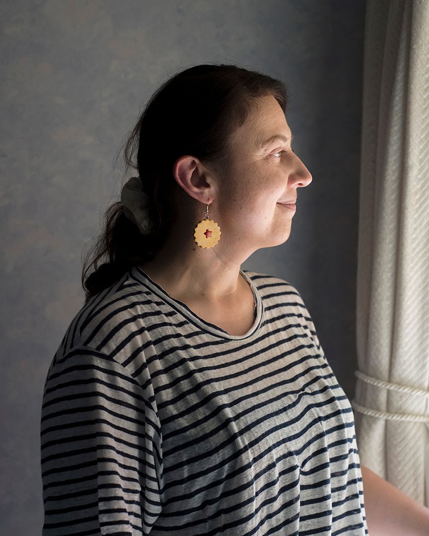 A woman stare out of her window, she is in profile, wearing jammy dodger earrings
