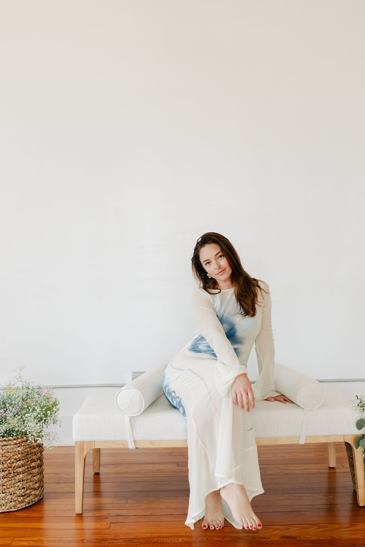 Person in denim outfit sitting on hardwood floor between two bright windows.