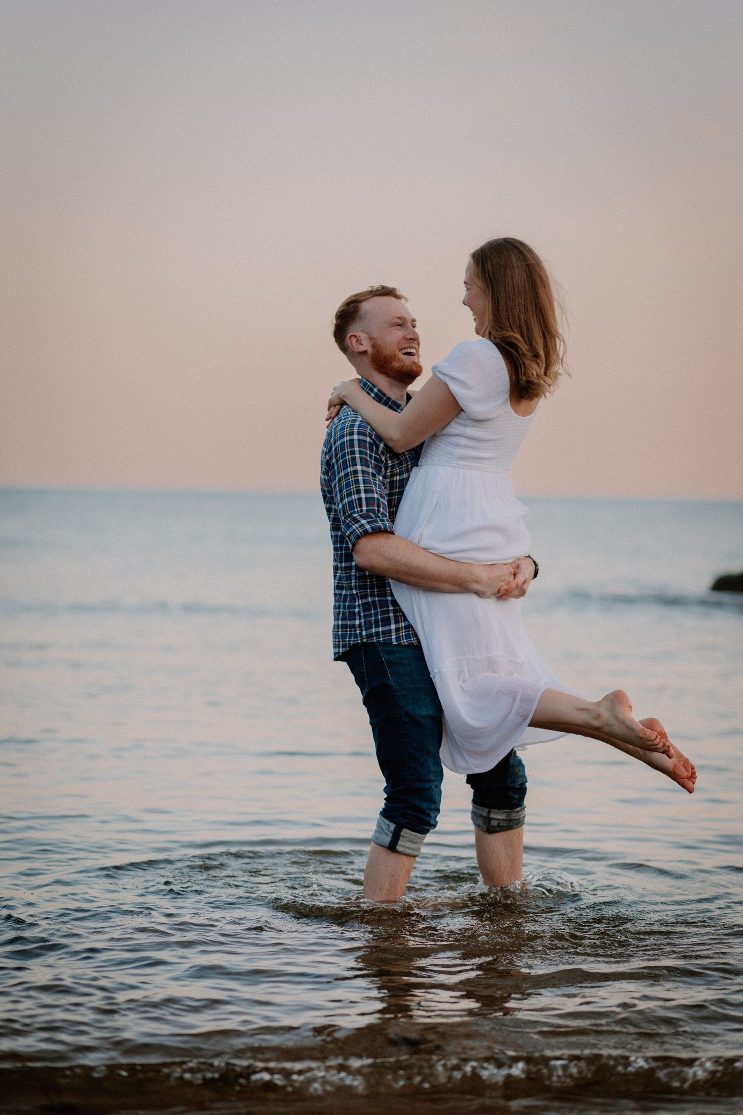 A couple shares an intimate moment while standing in shallow ocean water during golden hour.