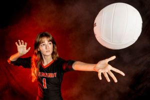 Volleyball player in black uniform preparing to serve against dramatic red smoky background.
