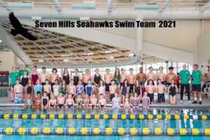 Large group photo of swim team members and coaches posing by indoor pool.