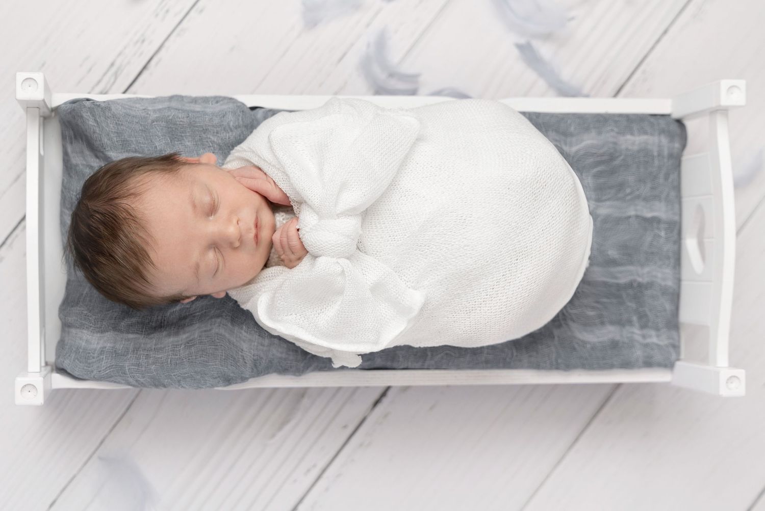 Sleeping baby wrapped in white swaddle on gray cushion.