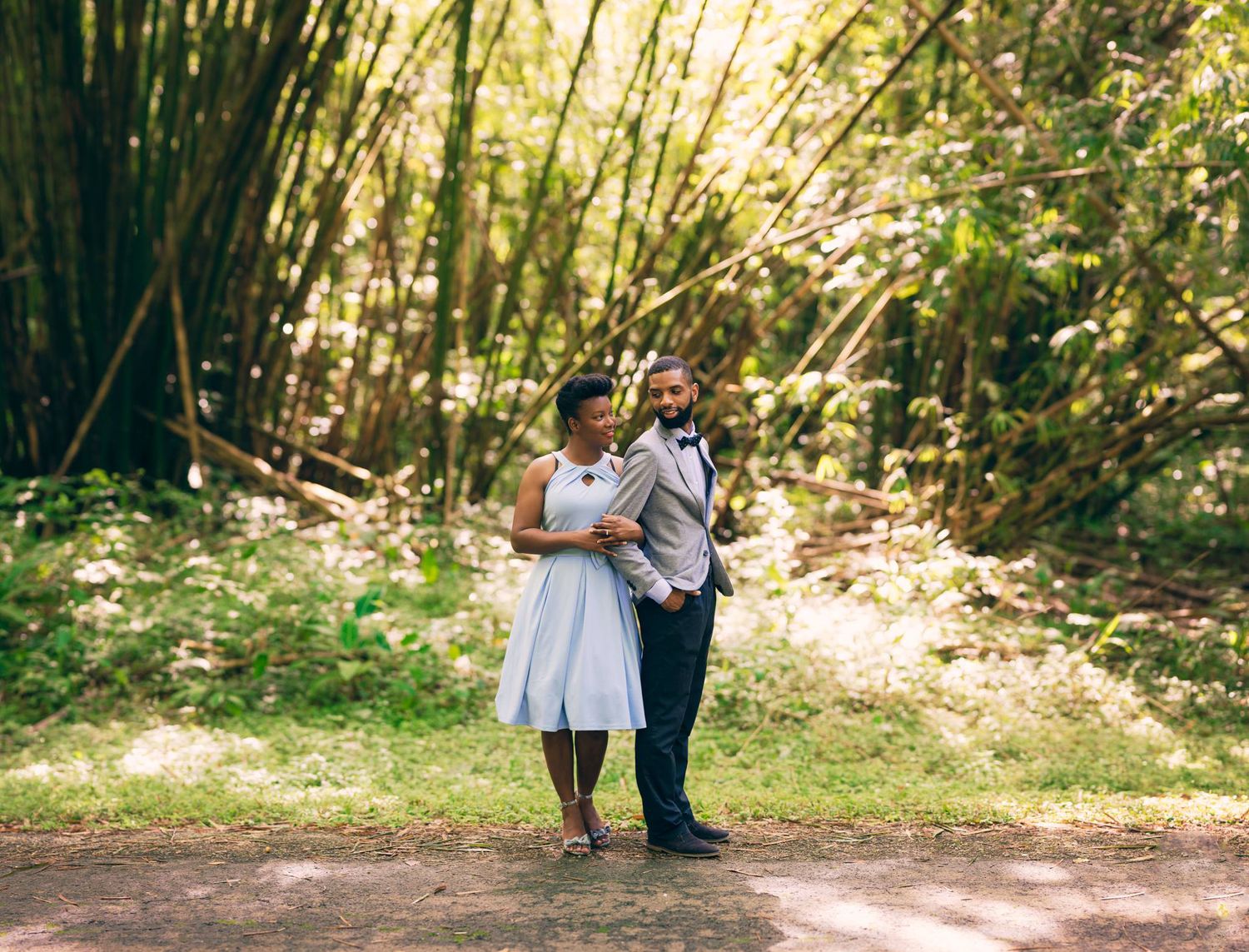 Romantic engagement photo in sunlit bamboo forest with couple in casual formal wear.