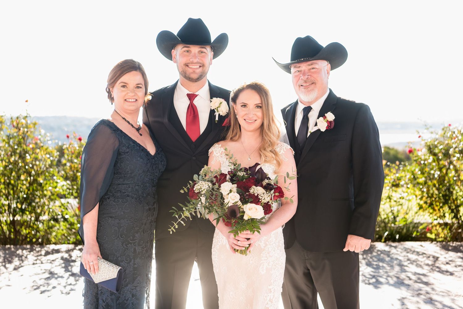 Wedding party in western attire poses together against sunny outdoor backdrop.