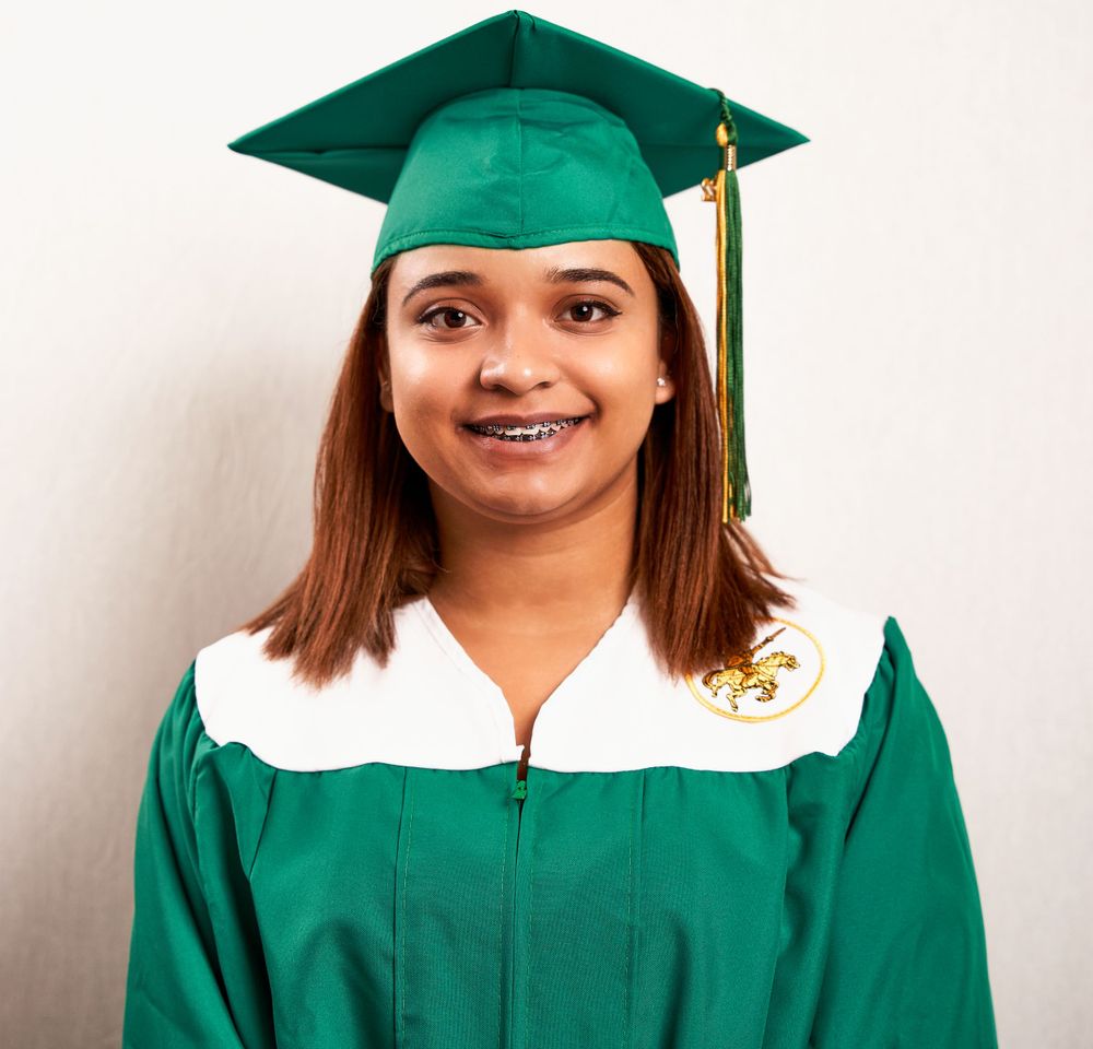 Graduate wearing emerald green graduation cap and gown with white trim.