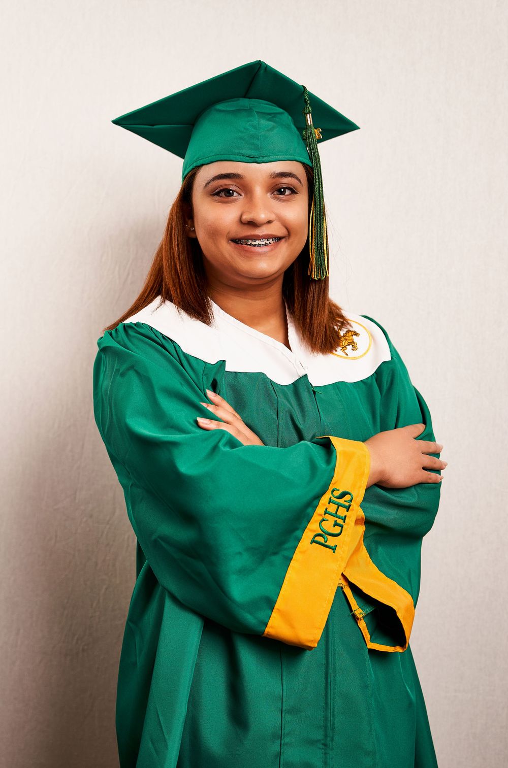 Graduate in green and white commencement regalia with gold sash posing against white background.