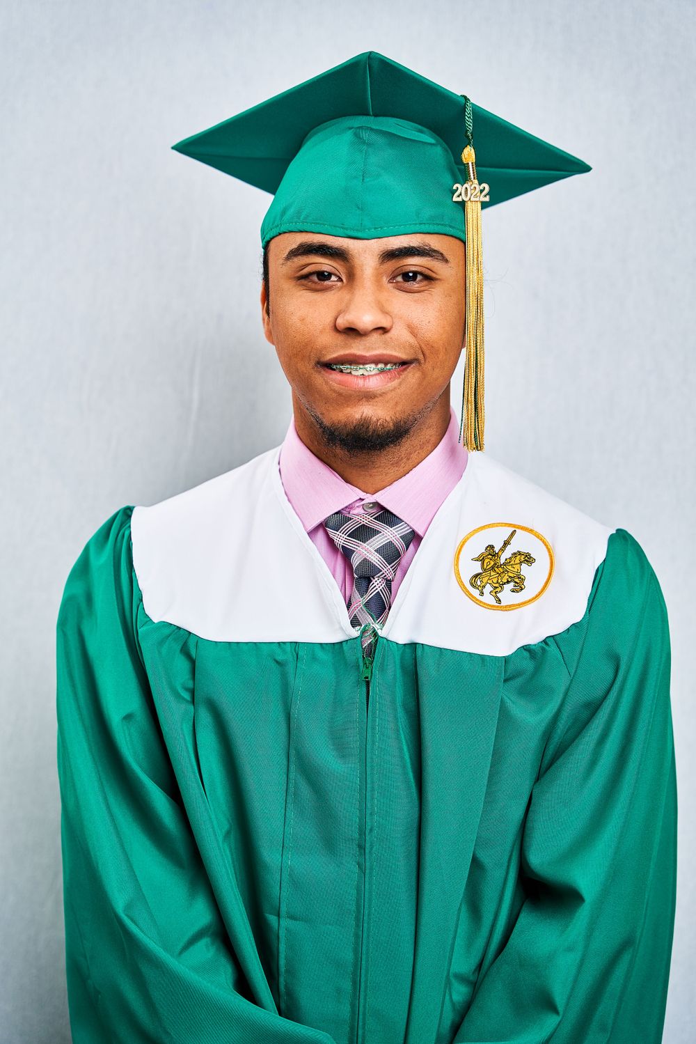 Graduate in green academic regalia with gold tassel and striped tie.