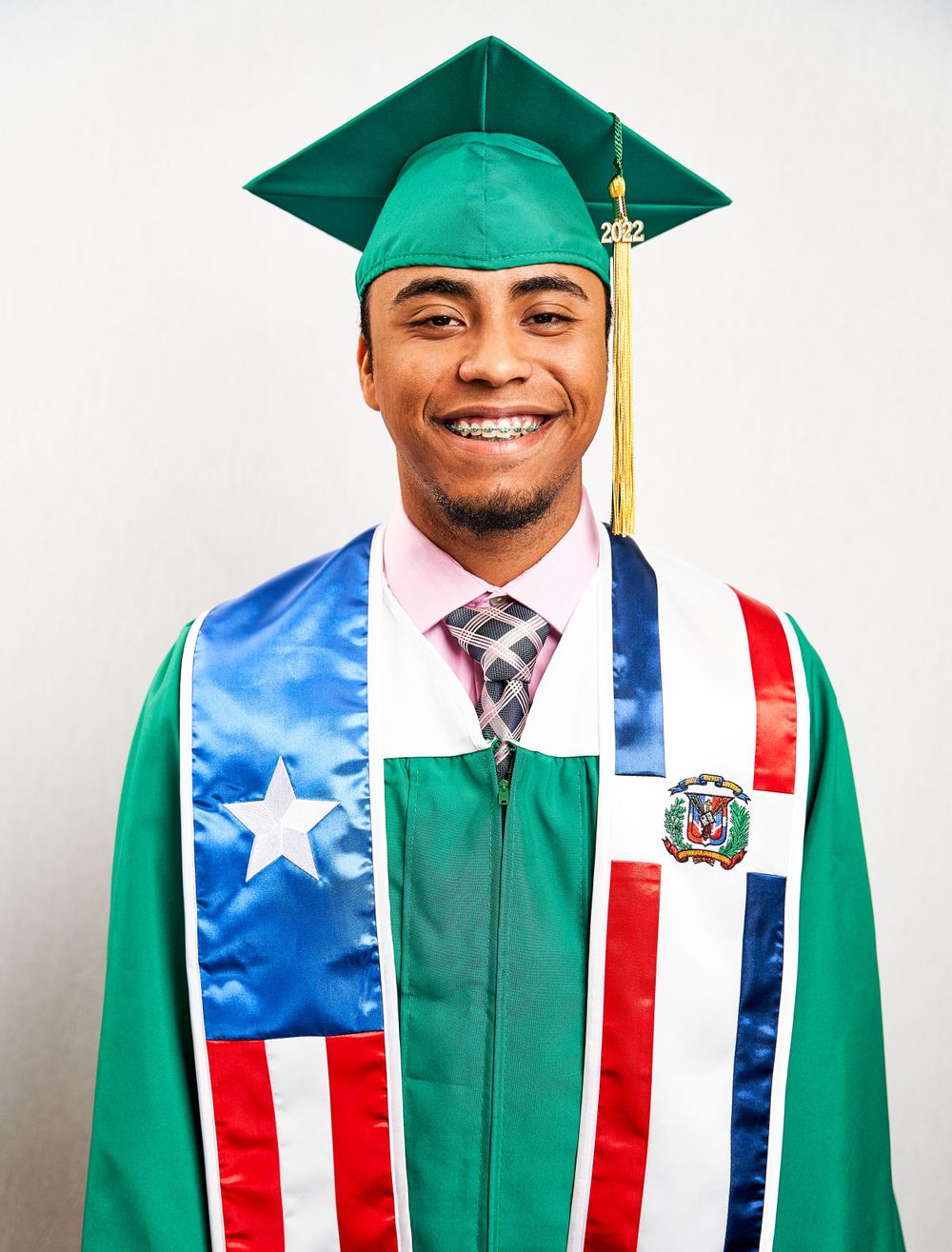 Graduate wearing green cap and gown with Puerto Rican and Dominican Republic flag stoles.