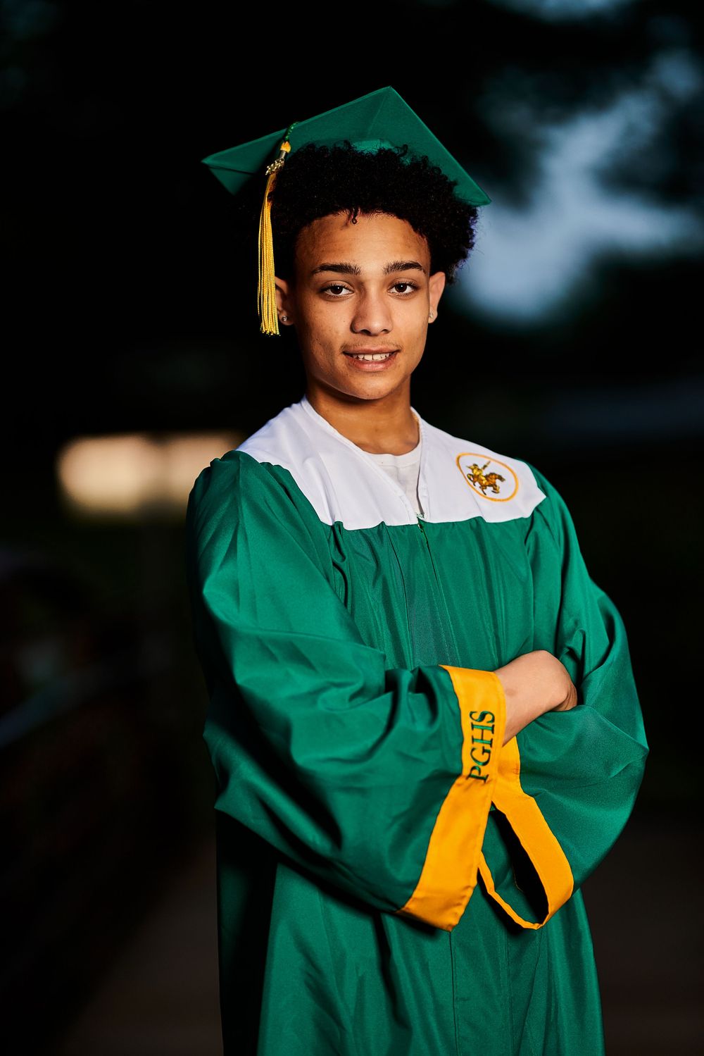 Graduate in emerald regalia poses outdoors with yellow tassel in evening light.