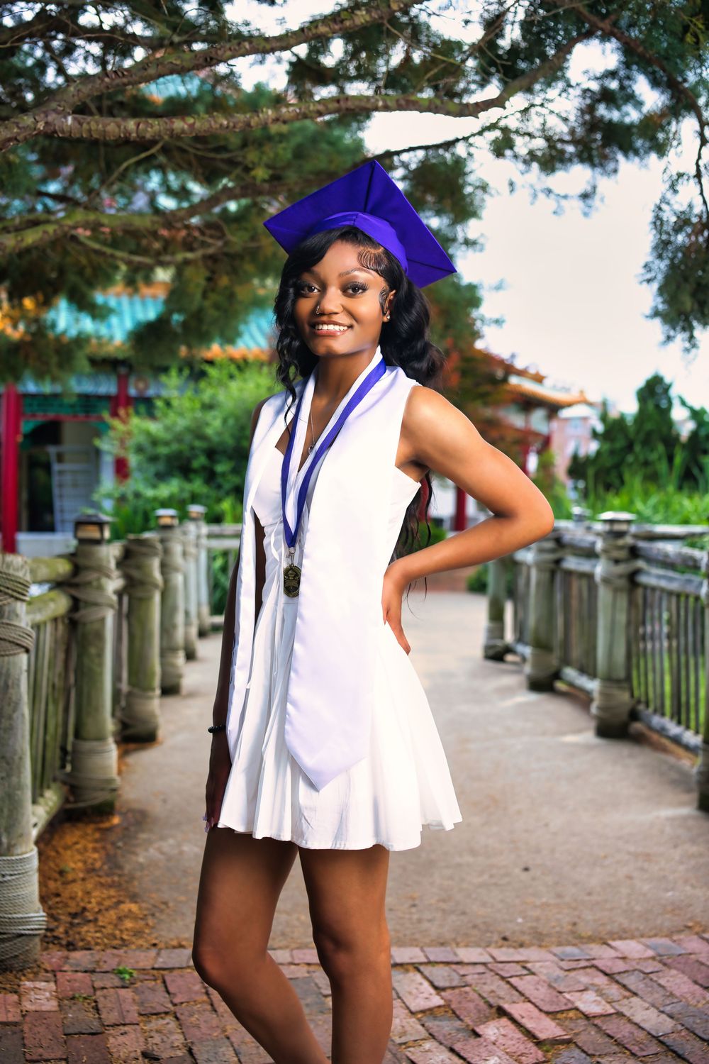 A series of fashion photos showing someone in a white sleeveless outfit and purple hat posing on a brick pathway near columns.