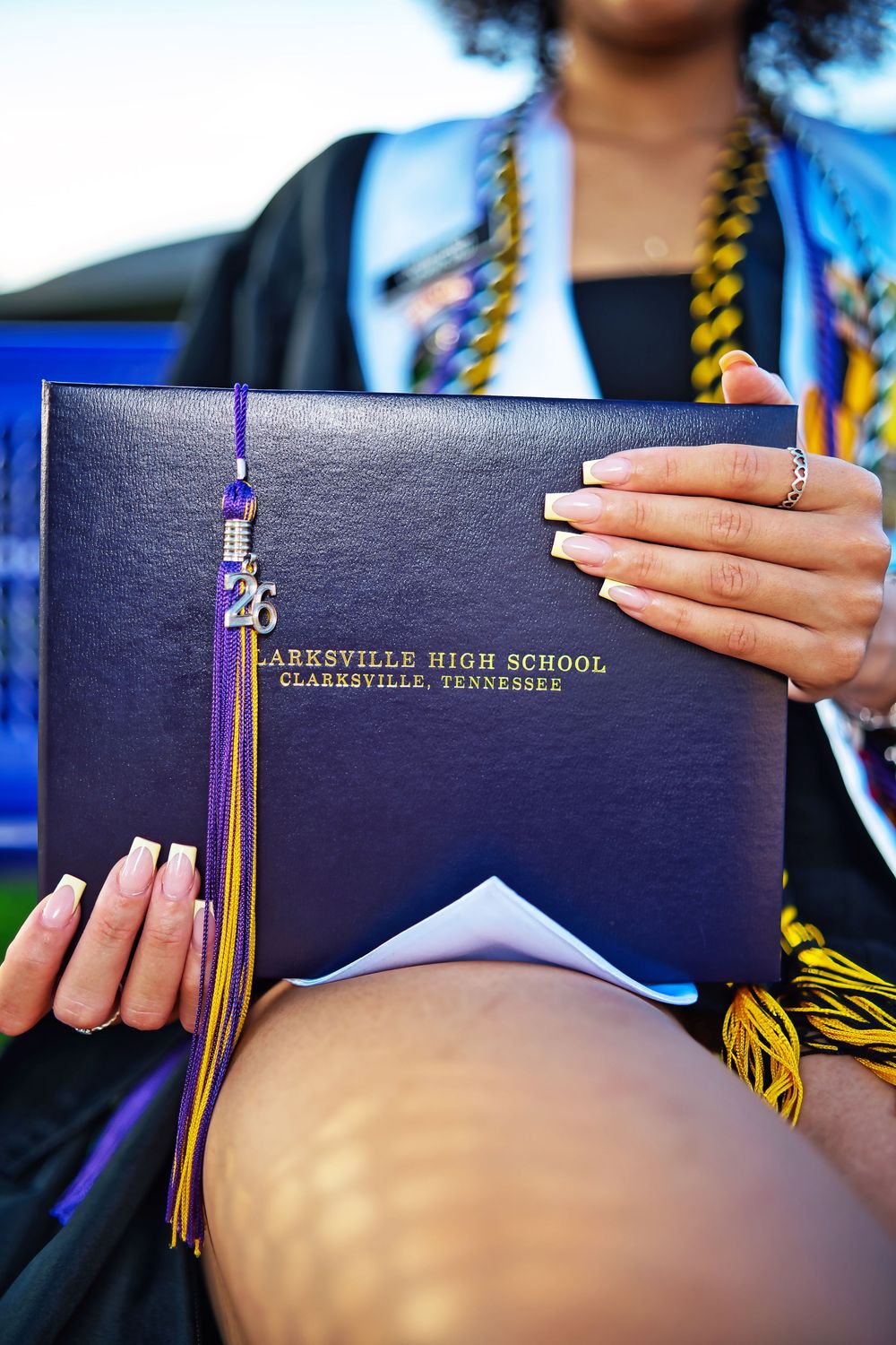 Graduate holding Clarksville High School diploma cover with purple and gold tassel at Tennessee graduation ceremony.