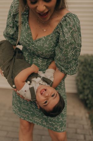 Woman in green floral dress playing with child upside down on brick patio.